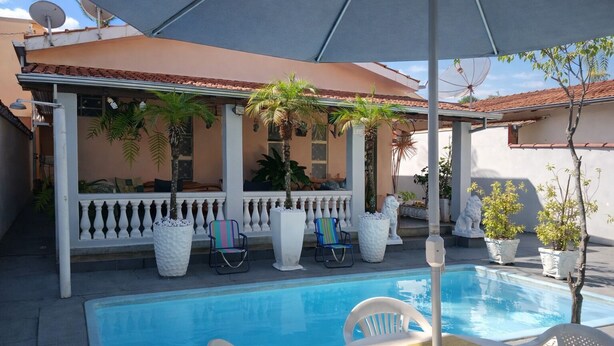 A pool area with a covered seating area, white chairs, and potted plants. - House in Rifaina, with swimming pool, close to the beach. (Rifaina)