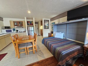 A compact room with a bed, a dining table with chairs, a kitchenette, and a small bathroom. - Park Place 229 -Parkside Escape -Downtown w/ view! (Cedar Key)