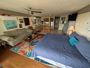A compact living space with a sofa, a bed with a blue cover, a dining table, a kitchen area, and a ceiling fan. - Park Place 229 -Parkside Escape -Downtown w/ view! (Cedar Key)