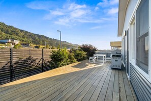 Eine Holzterrasse mit Gartenmöbeln, einem Grill und Blick auf eine hügelige Landschaft.
