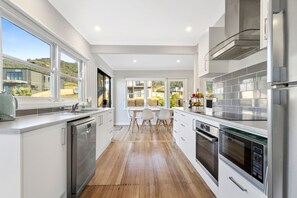 A modern kitchen with white cabinetry, stainless steel appliances, and a wooden floor. - Days by the Bay (Apollo Bay)