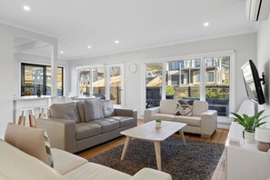 A modern living room with a grey sofa, a white sofa, a coffee table, and a TV mounted on the wall. - Days by the Bay (Apollo Bay)