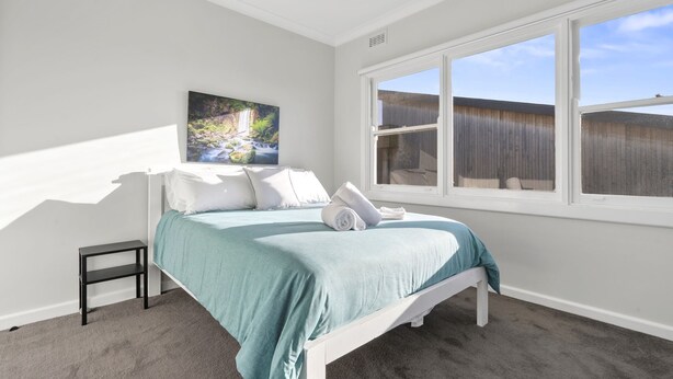 A bedroom with a bed, a window, a painting, and a small table. - Days by the Bay (Apollo Bay)