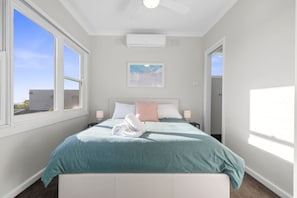 A bedroom with a bed, two bedside tables, a wall-mounted air conditioner, and a window with a view of the sky. - Days by the Bay (Apollo Bay)