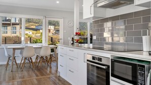 A modern kitchen with a view of a residential area, a dining area with chairs, and a clock on the wall. - Days by the Bay (Apollo Bay)