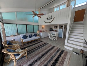 Een ruime woonkamer met een bank, stoelen, een eettafel en een keuken op de achtergrond.