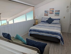 Een slaapkamer met een bed, kussens, een nachtkastje, een lamp en een raam.