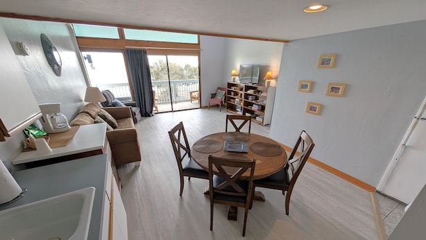 A modern living room with a round dining table, wooden chairs, a sofa, and a coffee machine. - Park Place -Parkside Dream -Downtown w/ Gulf View! (Cedar Key)