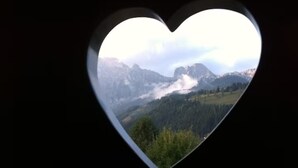 Ein herzförmiges Fenster mit Blick auf eine gebirgige Landschaft.
