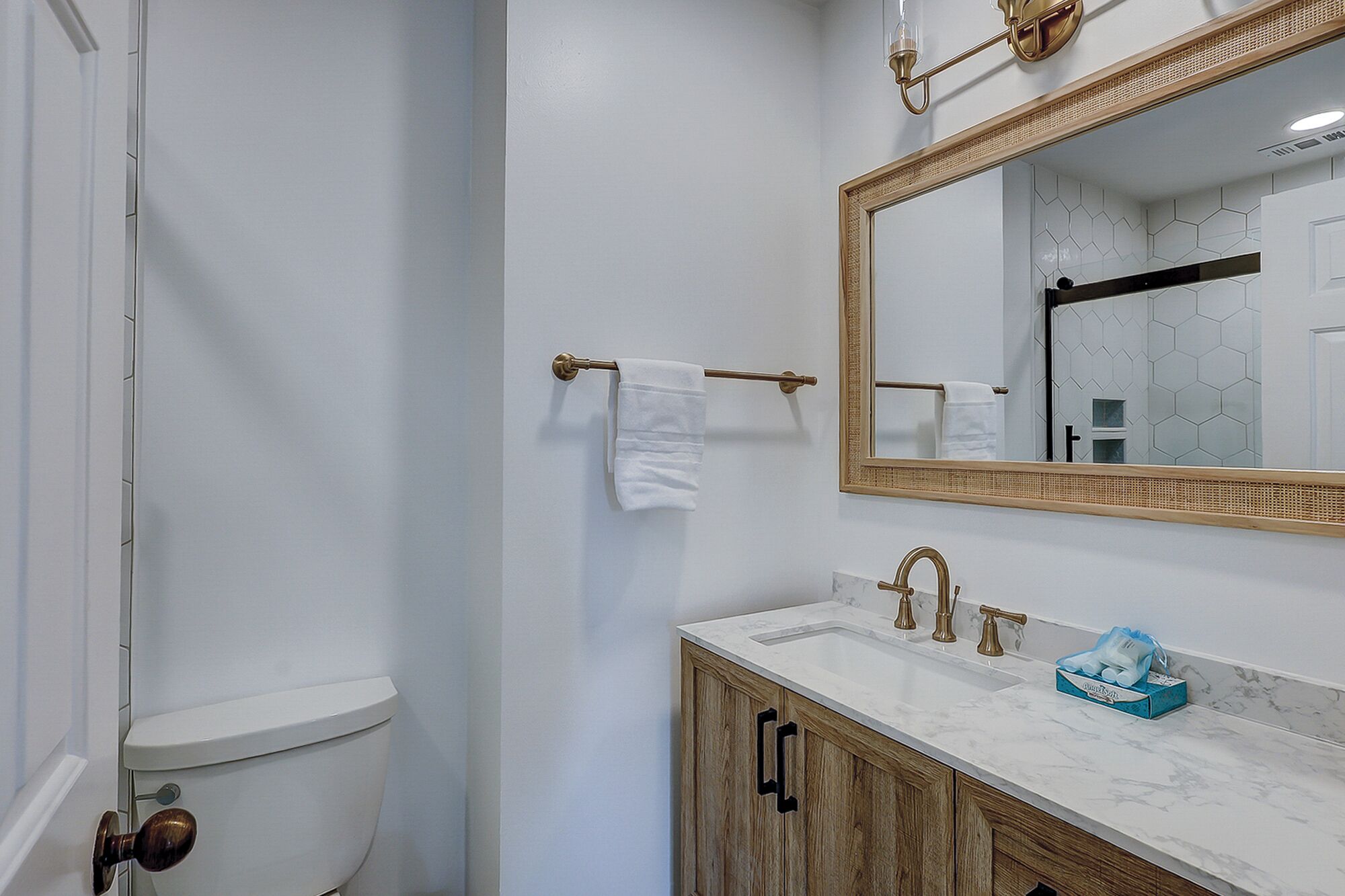 Une salle de bain comprenant des toilettes, un lavabo avec un plan de travail en marbre, un meuble en bois, un miroir avec un cadre décoratif et un porte-serviettes avec des serviettes blanches.