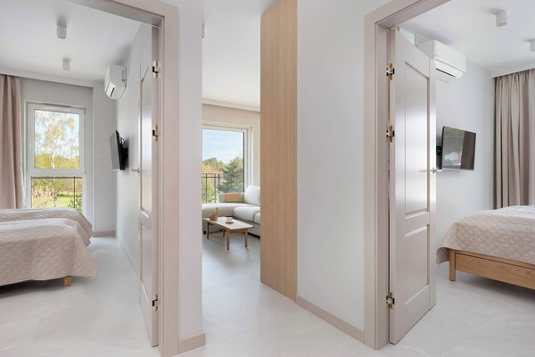 A hallway view shows the entryways to multiple bright rooms with light-colored wooden doors. The consistent flooring and neutral palette create a cohesive and harmonious interior design.