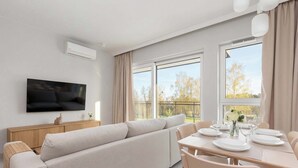 En moderne stue med en sofa, spisebord dækket til fire personer og et fladskærms TV monteret på væggen.