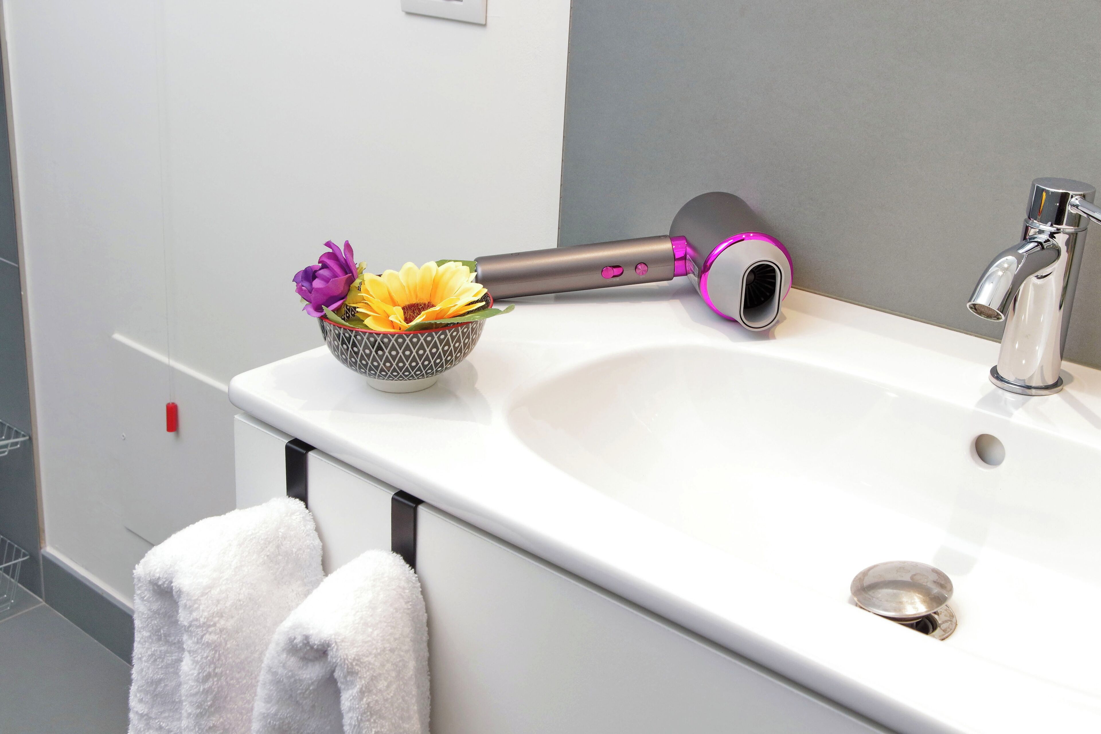 A bathroom with a white sink, a towel rack with two towels, a decorative bowl with flowers, and a hairdryer.