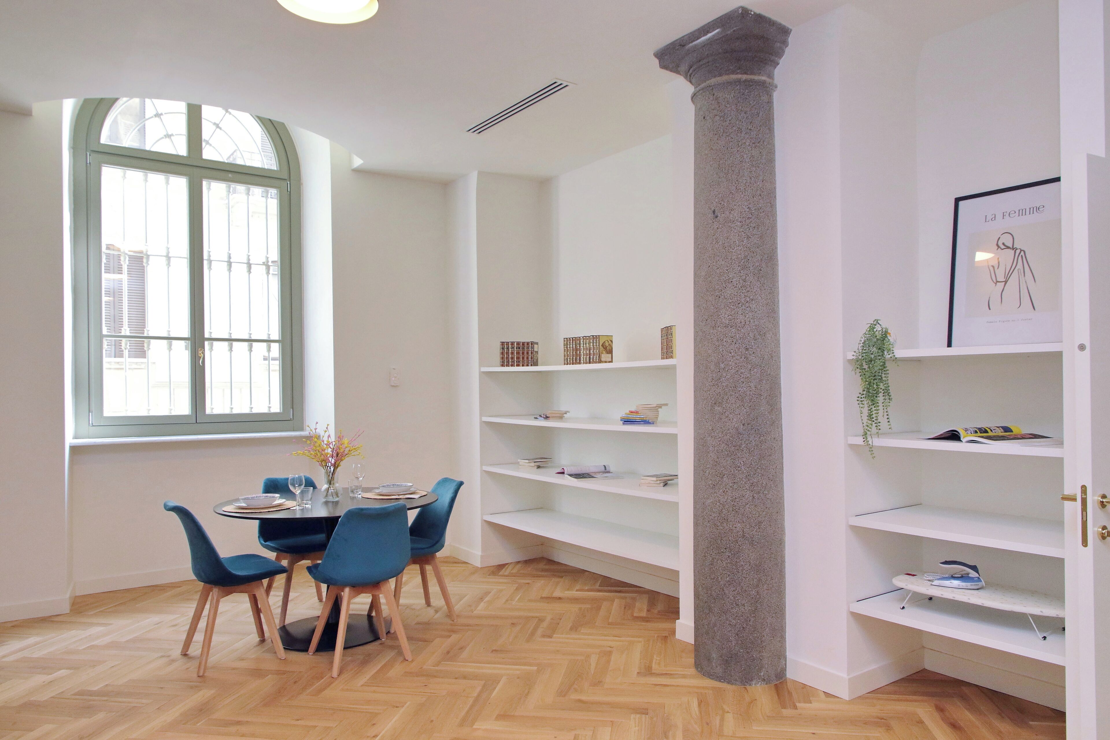 Ein Zimmer mit Esstisch, Stühlen, einem Fenster, Regalen und einer Säule.