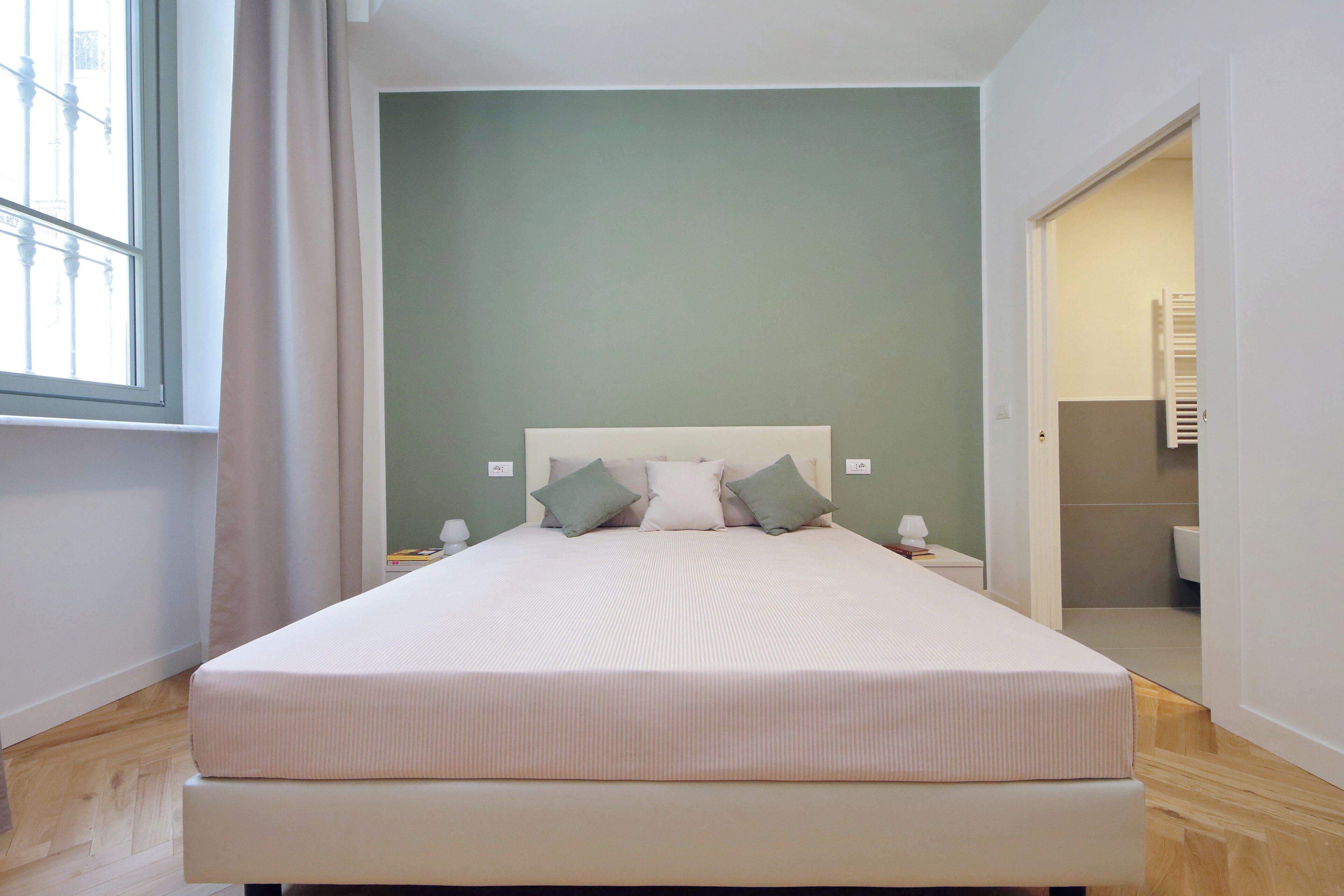 Un letto con testiera bianca, due cuscini, un comodino e una finestra con tende.