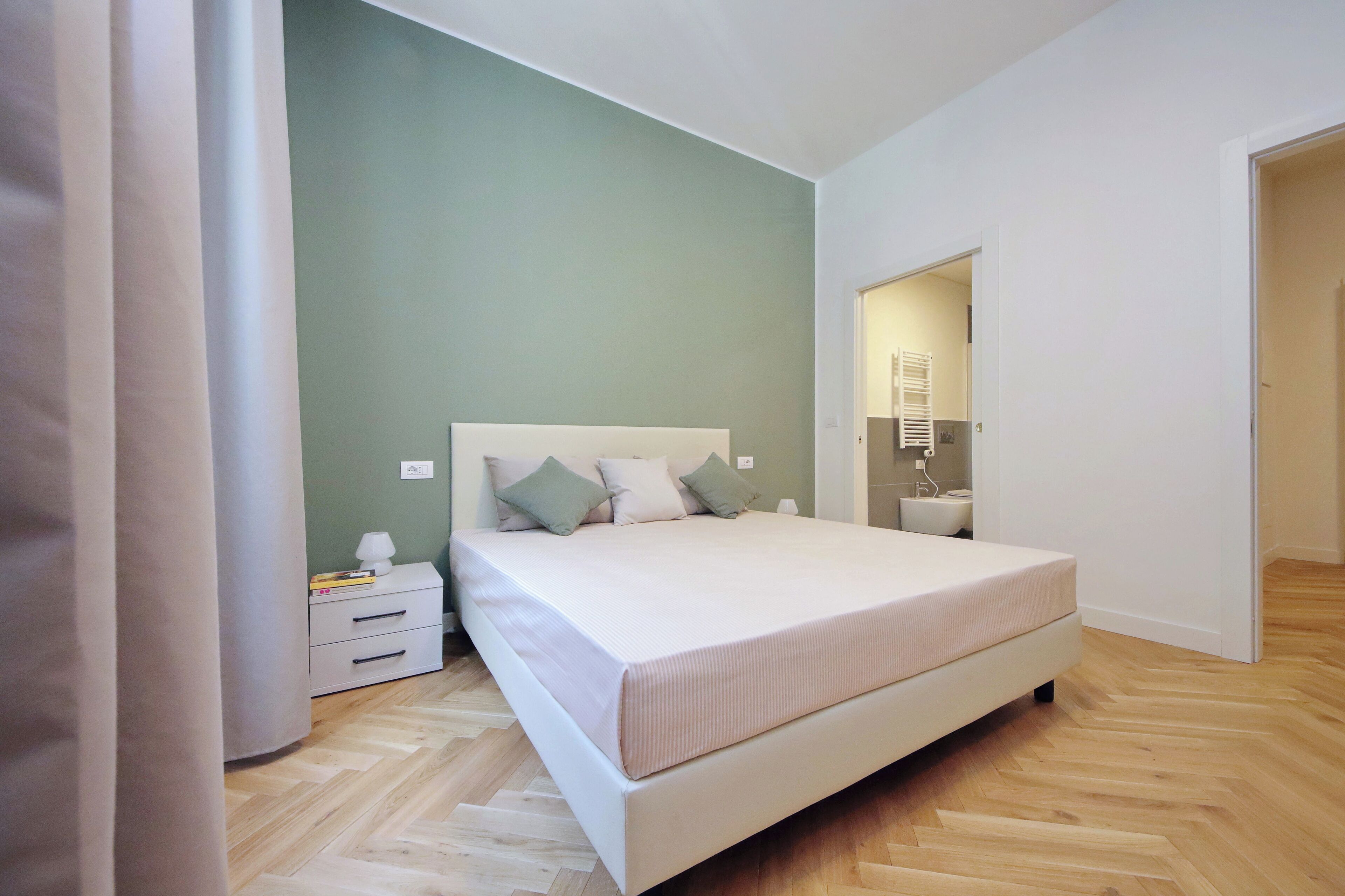 Ein Schlafzimmer mit Bett, Nachttisch, Lampe und Spiegel.