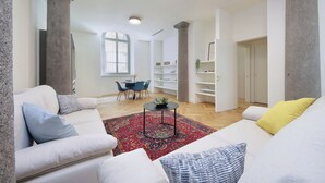A modern living room with a white sofa, a red patterned rug, and a dining area with a table and chairs.