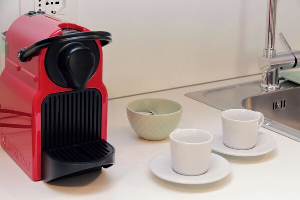 A red coffee machine, two white cups, and a green bowl on a kitchen counter.