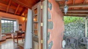 A wooden interior with a stone wall, a wooden door, a table with chairs, and a window with curtains. - Country House 'Gran Drago' with Sea View, Wi-Fi and Air Conditioning (Villa de Valverde)