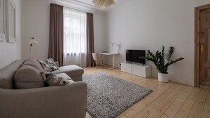 Ett modernt vardagsrum med en soffa, en tv, ett skrivbord och en krukväxt.