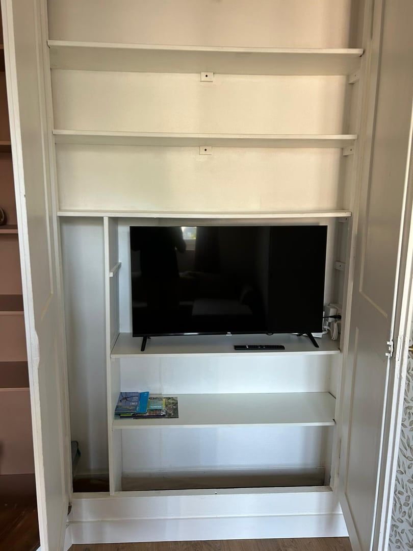 Un meuble de rangement blanc pour appareils multimédias, doté d’un téléviseur à écran plat, d’étagères intégrées et d’une petite table.