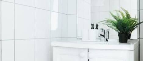 A bathroom with white tiled walls, a white sink with a mirror, and a potted plant on the counter.