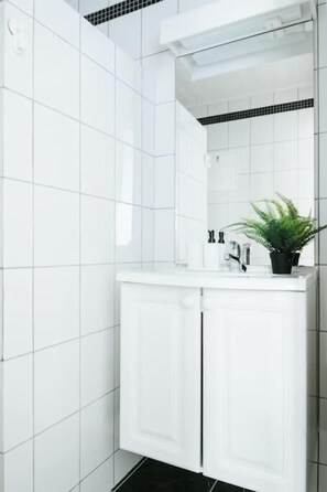 A bathroom with white tiled walls, a white sink with a mirror, and a potted plant on the counter. - City Center Apartment (Bergen)