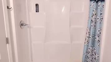 Une douche à l’italienne avec une porte en verre, un panneau de commande et un rideau de douche à motifs.