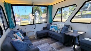 A modern RV interior with a sectional sofa, a small table, and large windows offering a view of the outside. - 🛥Stay Where The Water Meets Relaxation! (Panama City)