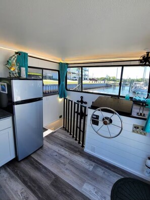 A compact kitchen with a refrigerator, a stove, and a window overlooking a marina.