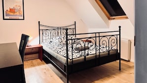 A bedroom with a black metal bed frame, a wooden desk, and a small window.