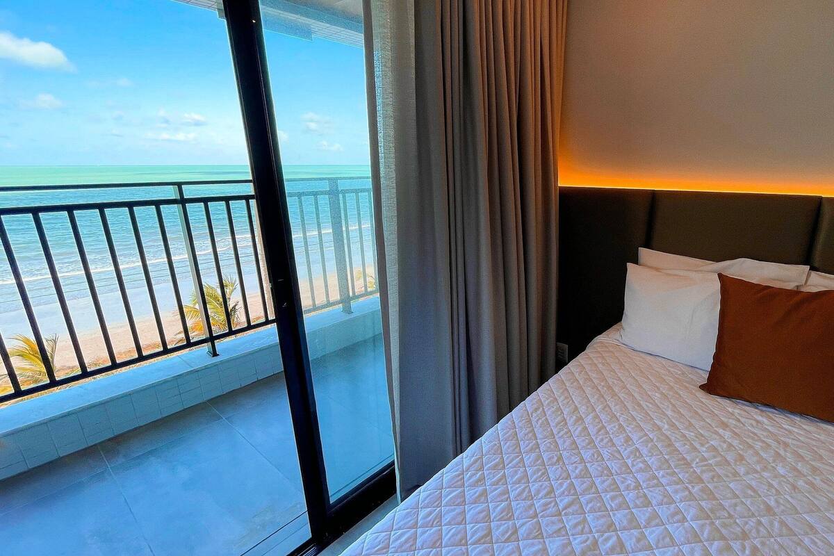 Une chambre d’hôtel avec un lit, une vue sur l’océan et un balcon doté d’une balustrade.