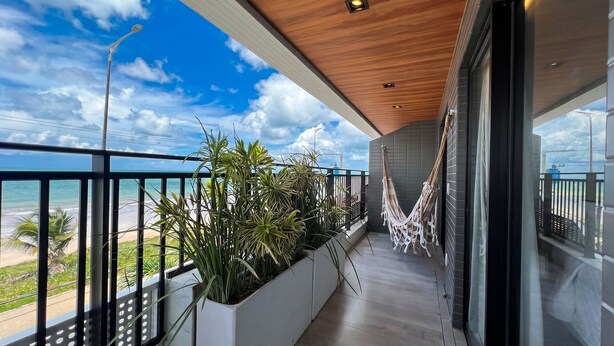 A balcony with a view of the ocean, potted plants, and a hammock.