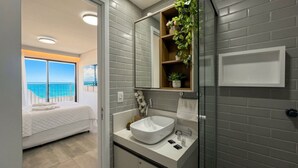 A modern bathroom with a large mirror, white sink, and a potted plant.