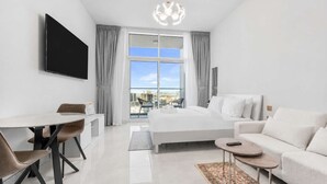 A modern hotel room with a bed, a desk, a sofa, and a large window with a city view. - StayShort - Premium New Arjan Studio - sleeps 3 (Arjan)