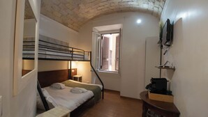 A compact room with a bunk bed, a small desk, a TV mounted on the wall, and a window with shutters. - Colosseum: Exposed Brick Double & Private Bath (Roma)