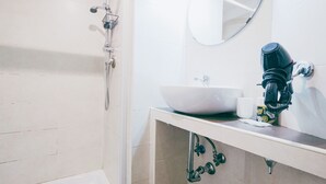 A bathroom with a white sink, a mirror, a hairdryer, and a shower. - Colosseum: Exposed Brick Double & Private Bath (Roma)