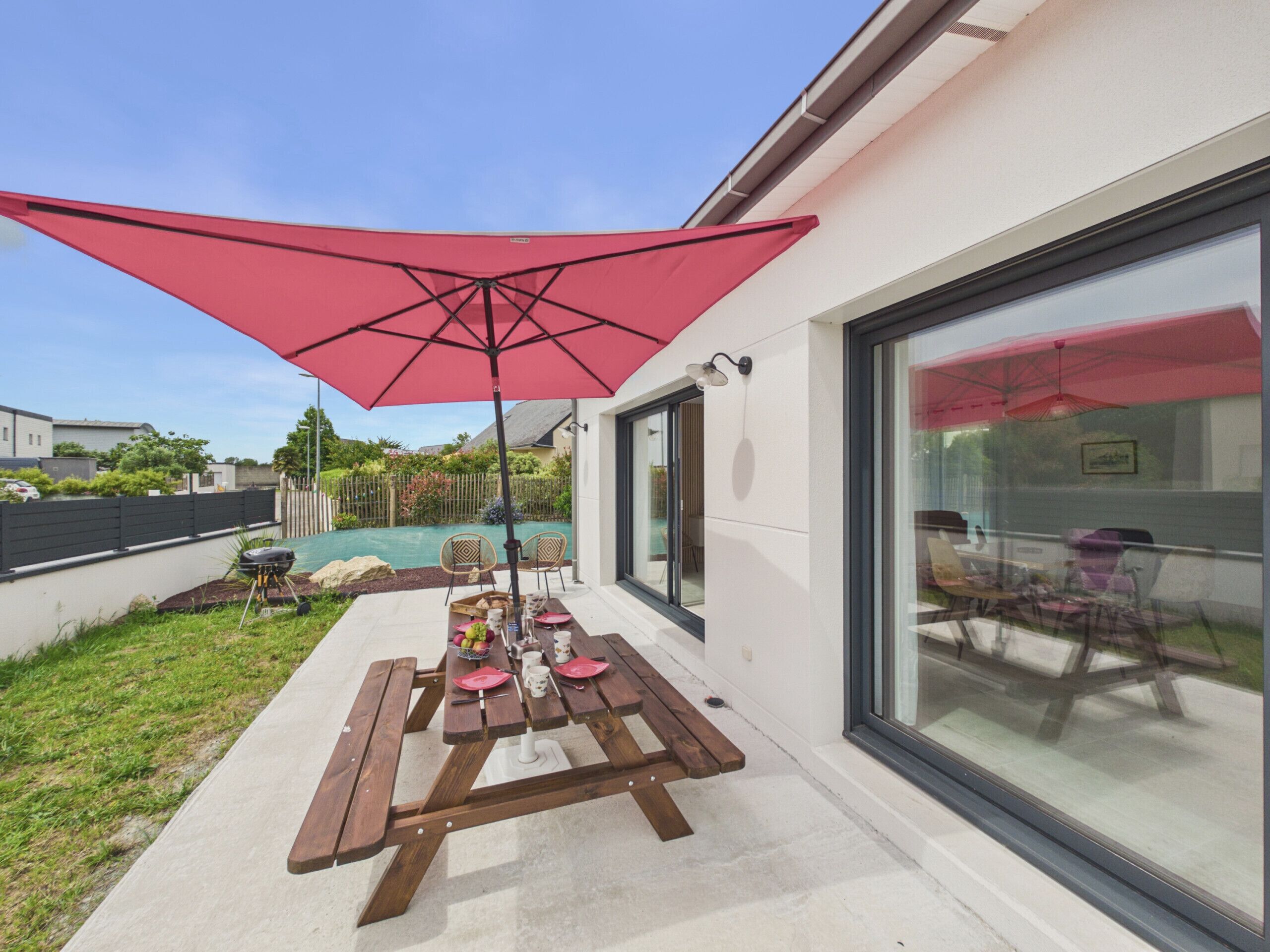 Une terrasse avec une table en bois, des chaises et un parasol rouge.