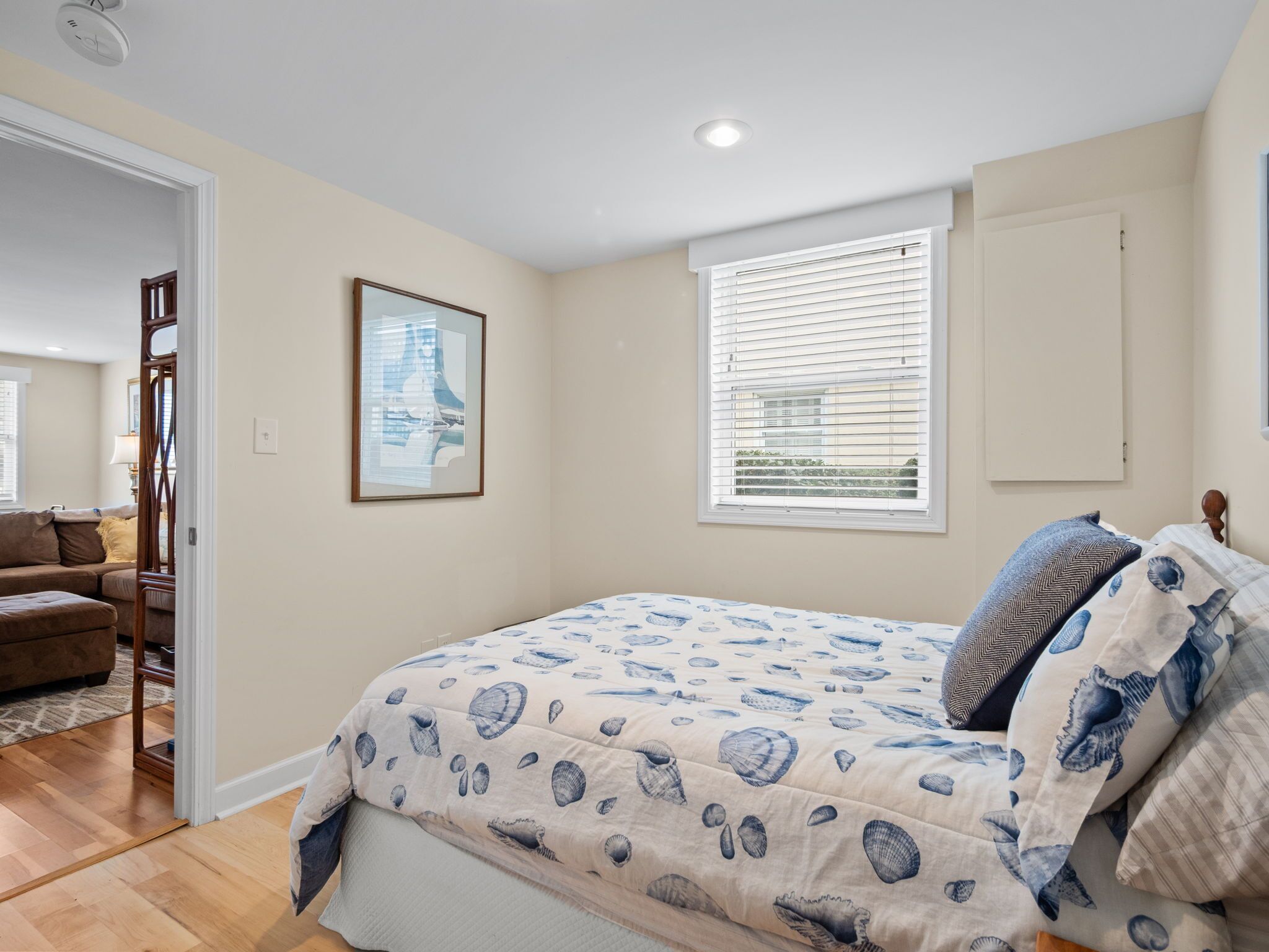 A bedroom with a bed, a window with blinds, a door, and a framed picture on the wall.