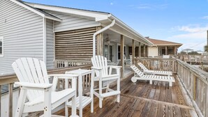 Een houten terras met witte Adirondack-stoelen en een overdekt gedeelte met een plafondventilator.