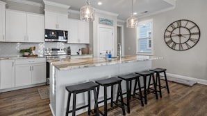 A modern kitchen with white cabinets, a large island with bar stools, a stainless steel oven, and pendant lighting. - Beautime-Pet Friendly Home in Downtown Beaufort, NC (Beaufort)