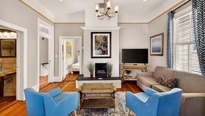 Een woonkamer met een open haard, televisie, bank en blauwe fauteuils.