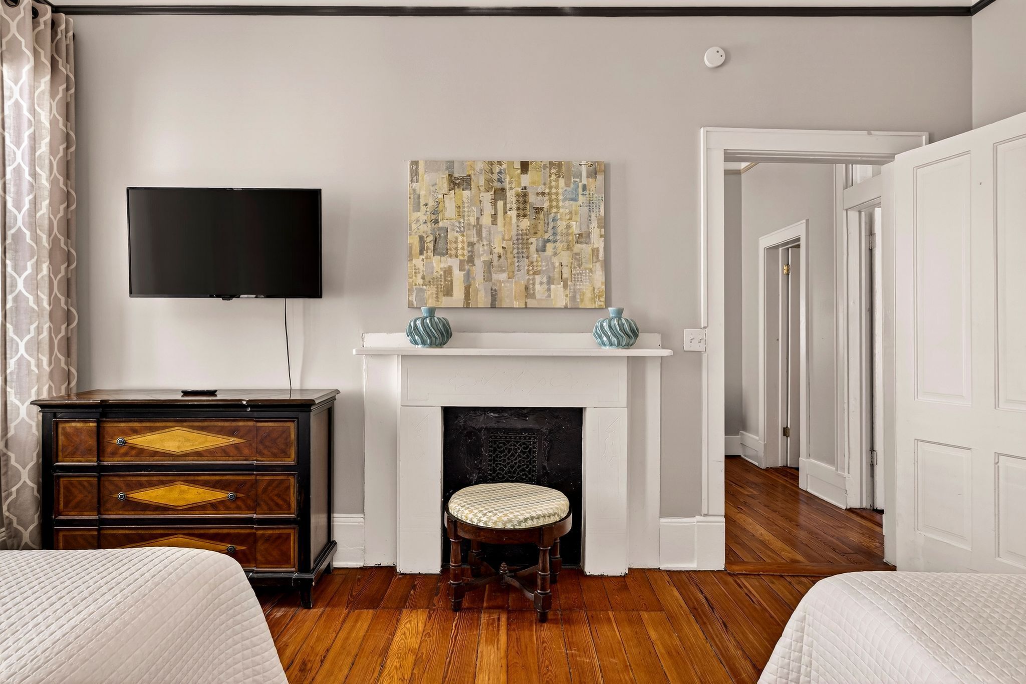 A bedroom with a bed, a dresser, a television, a fireplace, and a painting.