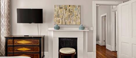 A bedroom with a bed, a dresser, a television, a fireplace, and a painting.