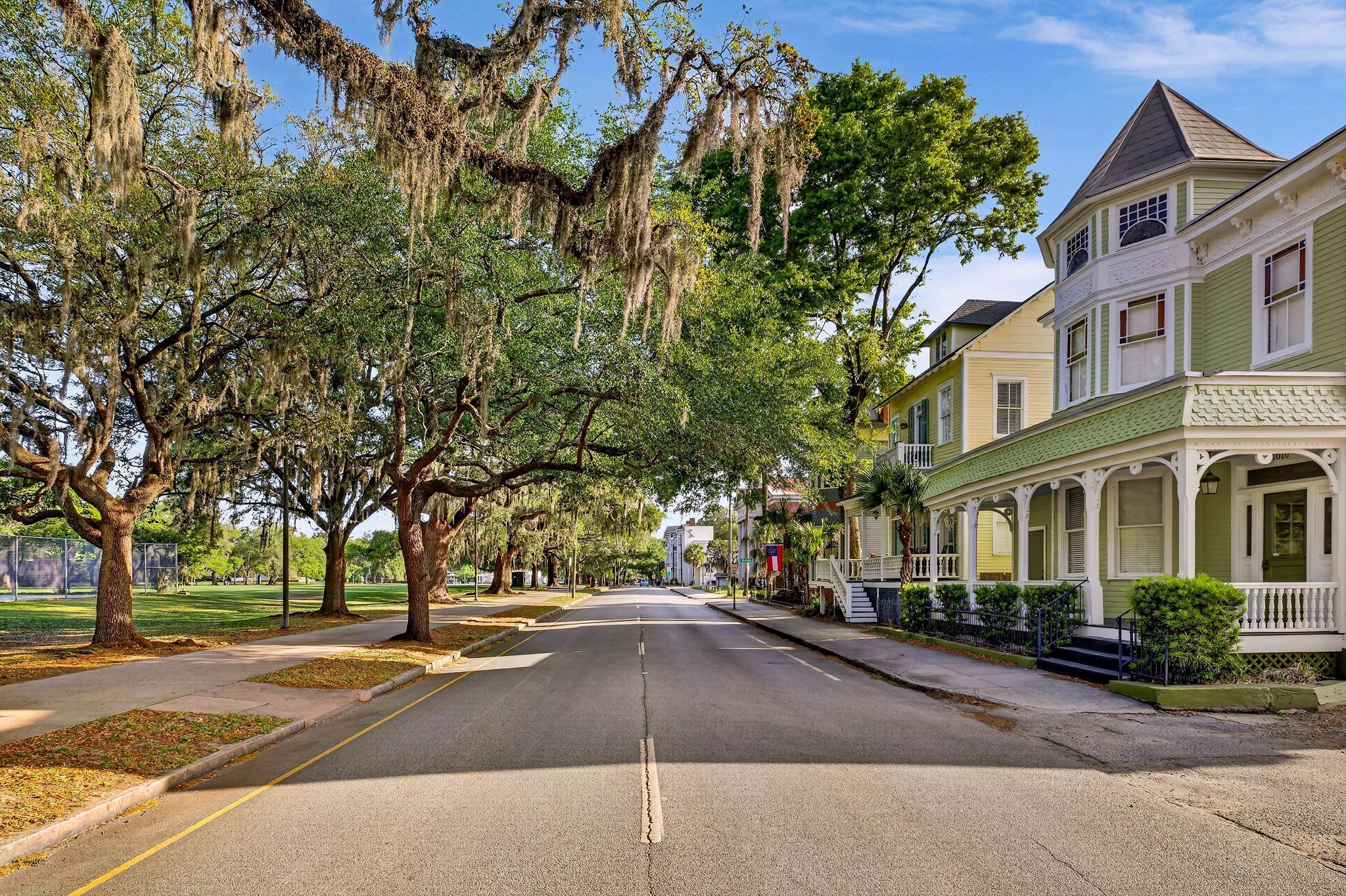 A street lined with historic houses, a clear road, and mature trees with Spanish moss.