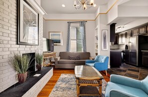 A modern living room with a sofa, blue armchair, and a glass-top coffee table. - Bright 2BR Historic Apartment Overlooking Forsyth Park by Lucky Savannah (Savannah)