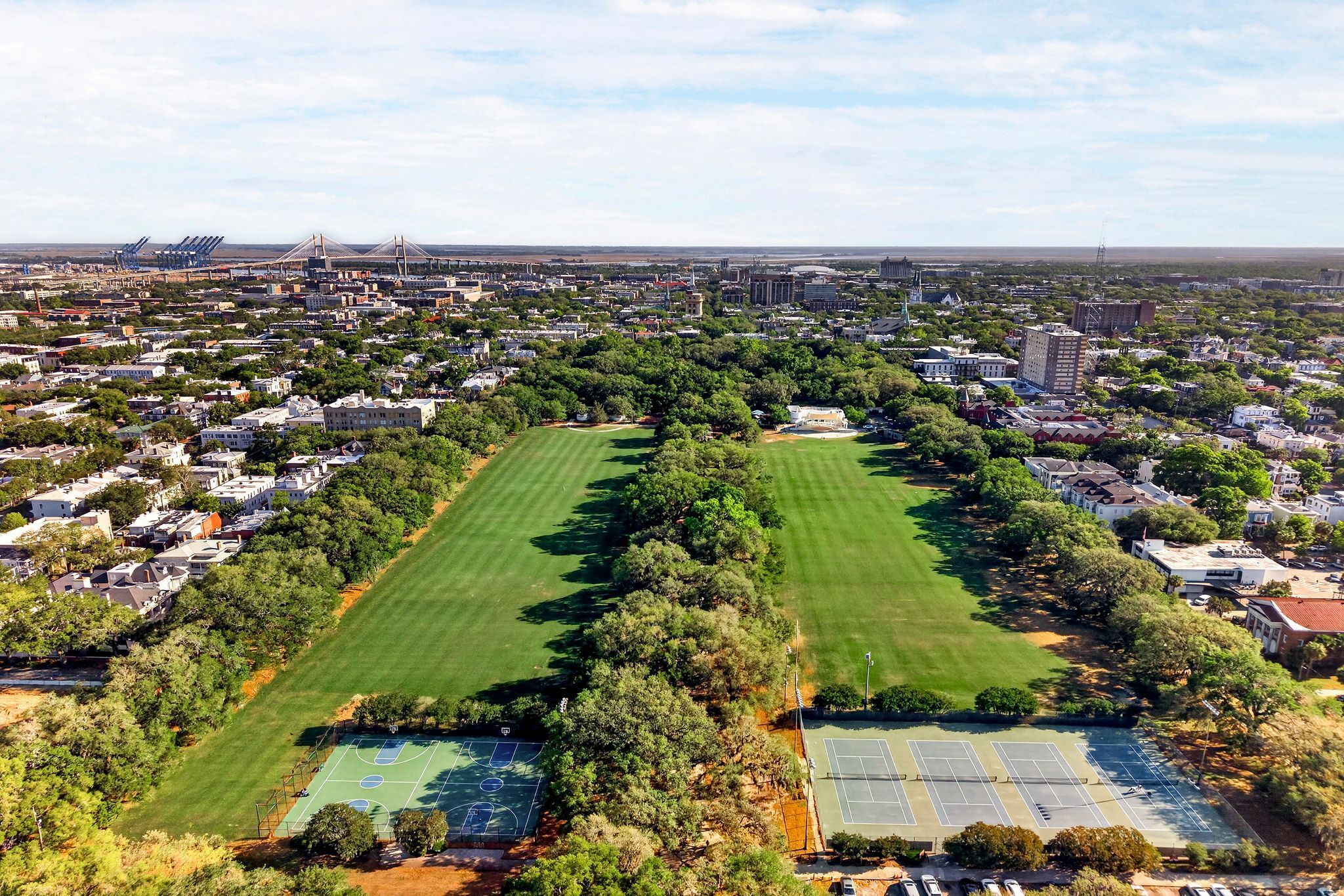 An aerial view of a residential area with multiple tennis courts, a large green park, and surrounding buildings.