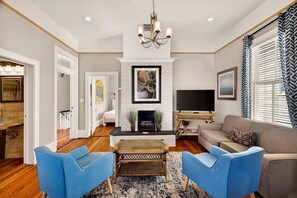 A living room with a fireplace, television, sofa, and blue chairs. - Bright 2BR Historic Apartment Overlooking Forsyth Park by Lucky Savannah (Savannah)