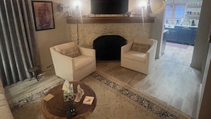 Un salon avec deux fauteuils blancs, une table basse, une cheminée et un téléviseur fixé au-dessus.