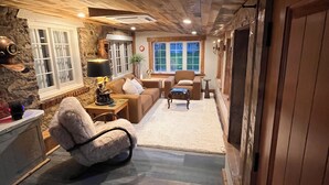 Un salon chaleureux avec une cheminée, un mur en pierre et un plafond en bois.